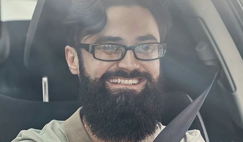 A man with eyeglasses smiling while driving a car.
