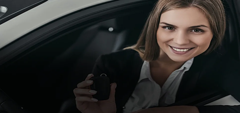A blonde hair woman holding a car key while inside a white car.
