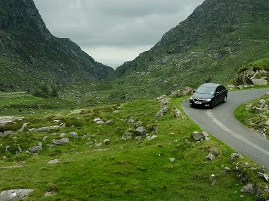 Black car driving down a green mountain slope.